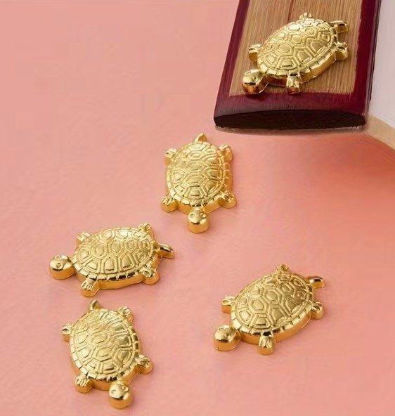 Four decorative golden turtle charms on a pink background.